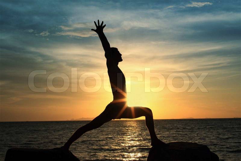 Silhouette of perfect body man act yoga on the rock with sea sunset background, stock photo