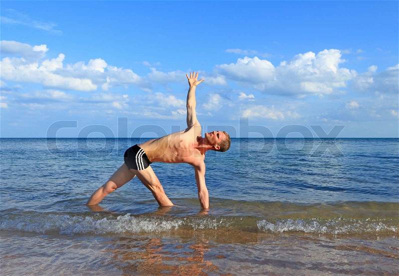 Man doing yoga Twist triangle pose by the beach at morning sunlight , stock photo