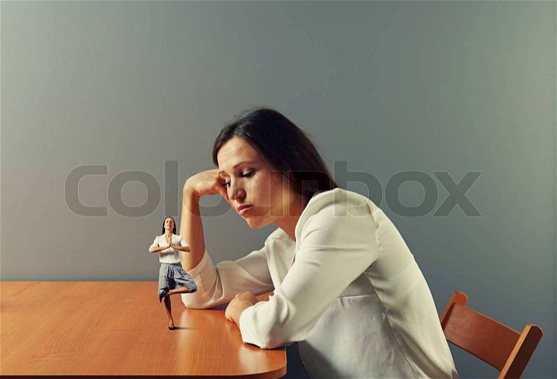 Sorrowful businesswoman looking at small meditation woman, stock photo