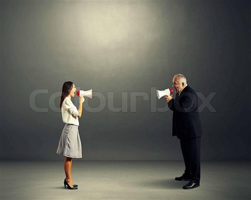 Senior man and young woman screaming with megaphone in dark empty room, stock photo