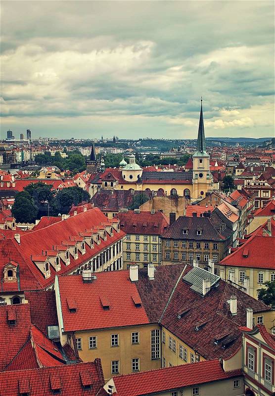 Vertical oriented image of typical buildings with red roofs in old city under cloudy sky in Prague, Czech Republic (toned), stock photo