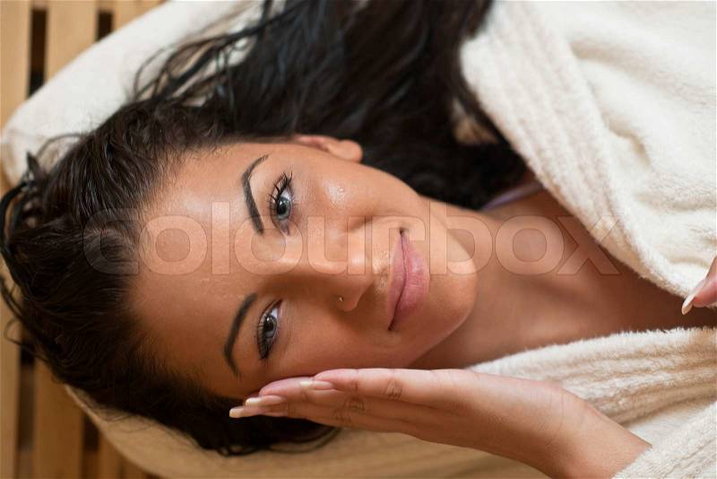 Pretty Young woman take a steam bath treatment at finish wooden sauna while wearing white towel, stock photo