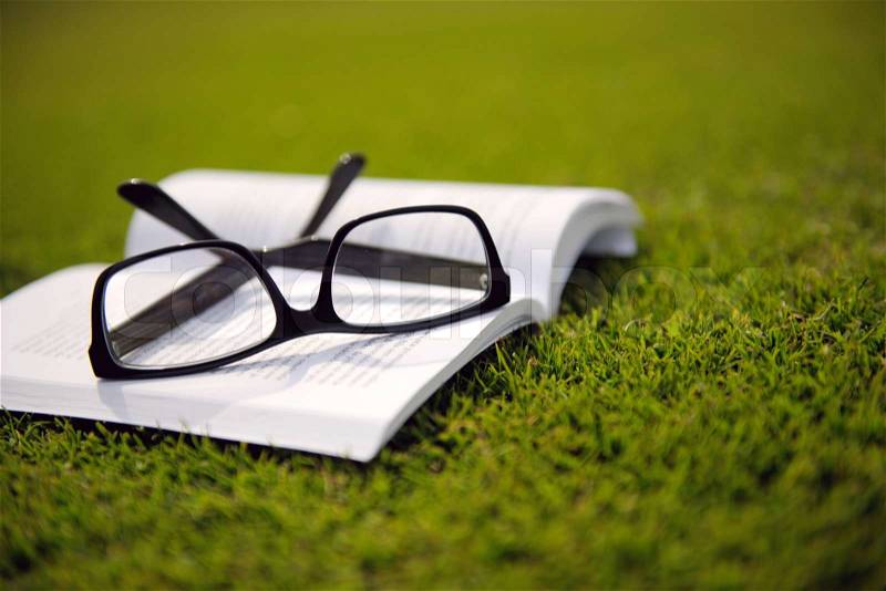 Glasses on a book outside with grass inbbacground, education relax and study concept, stock photo
