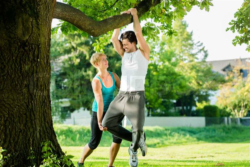 Young woman and personal trainer exercising chins or pull ups in City Park under summer trees for sport fitness, stock photo