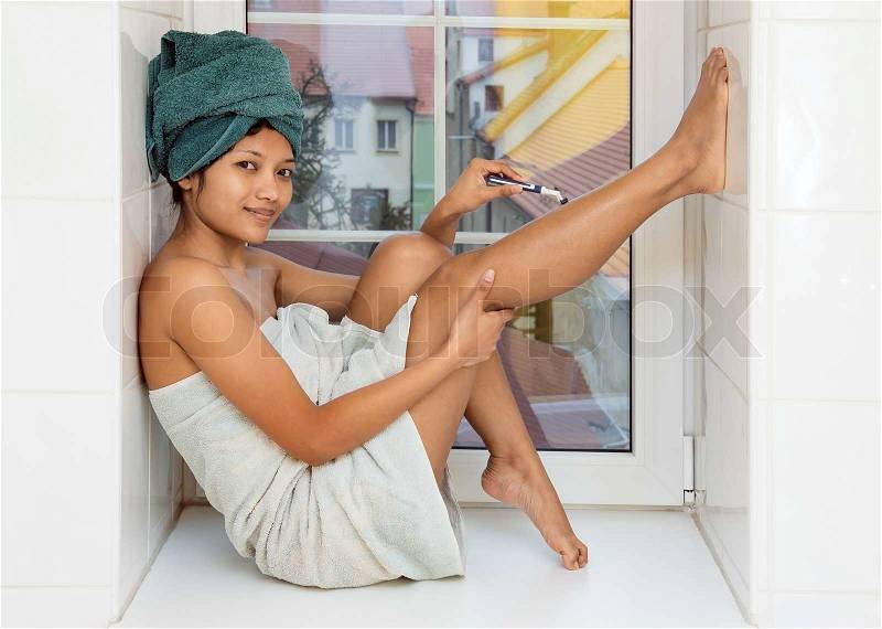 Woman sitting on the windowsill and shaves her legs, stock photo