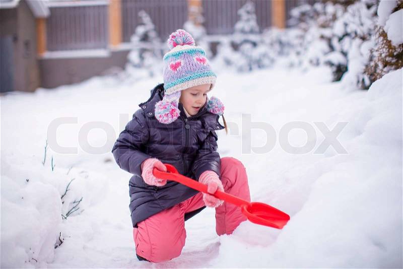 Little adorable girl play with snow shoveling on a winter day, stock photo
