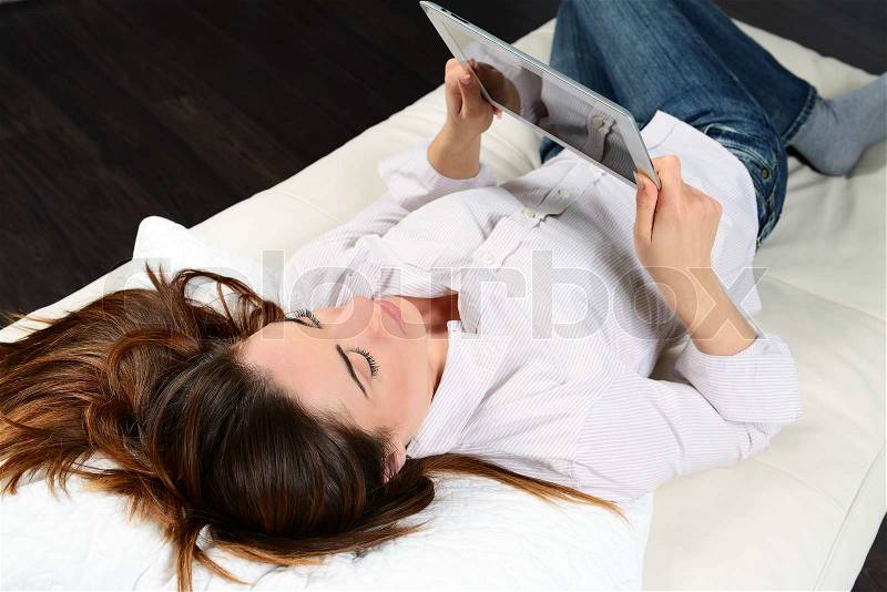 Young woman lying on sofa with electronic pad, stock photo