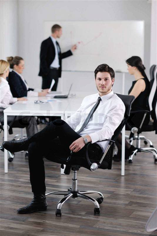 Portrait of a handsome young business man with people in background at office meeting, stock photo