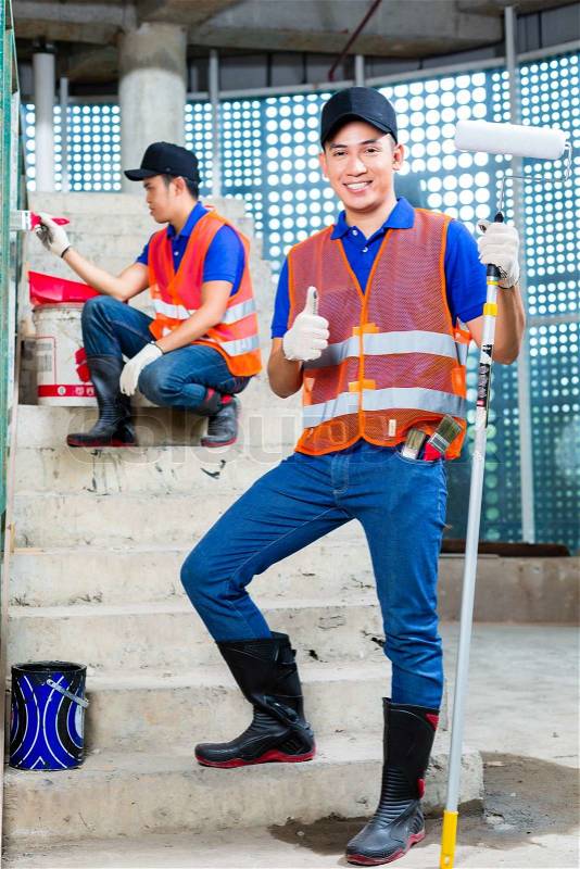 Asian Indonesian painter paint with a brush, paint roller, color and tools in gumboots or rubber boots and protection gloves the walls of a tower building or construction site, stock photo