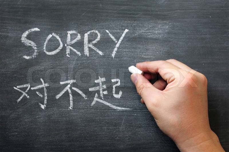 Sorry - word written on a smudged blackboard with a Chinese translation, with a hand holding chalk, stock photo