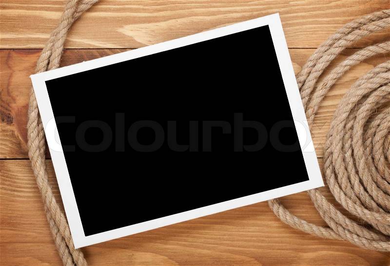 Blank photo frame with ship rope over wooden background, stock photo