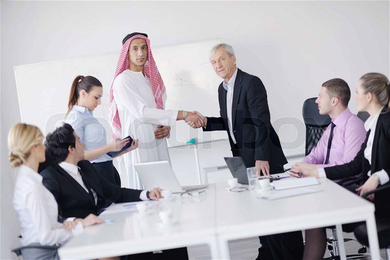 Business meeting - Handsome young Arabic man presenting his ideas to colleagues and listening for ideas for success investments at bright modern office room, stock photo