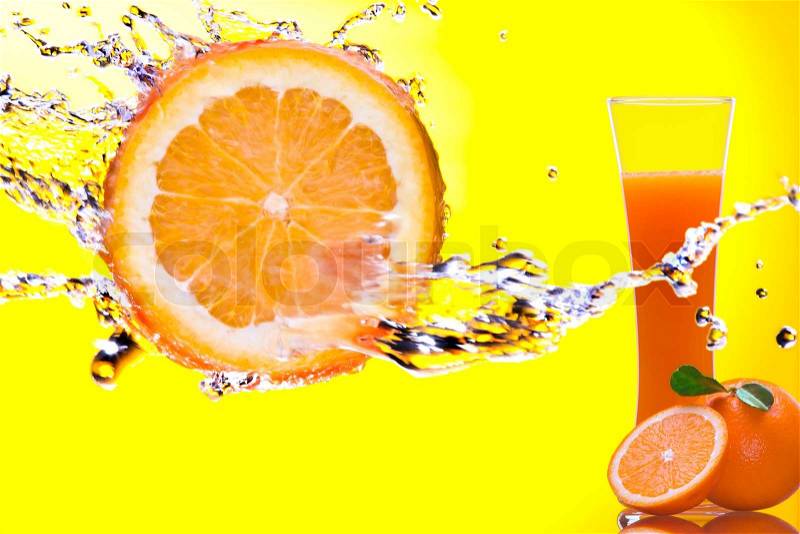 View of piece of orange getting splashed and glass of juice on back, stock photo