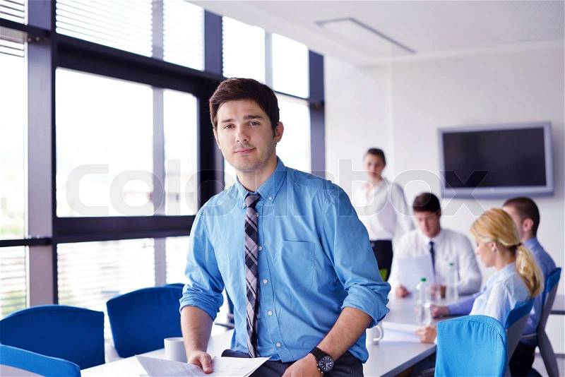 Portrait of a handsome young business man on a meeting in offce with colleagues in background, stock photo