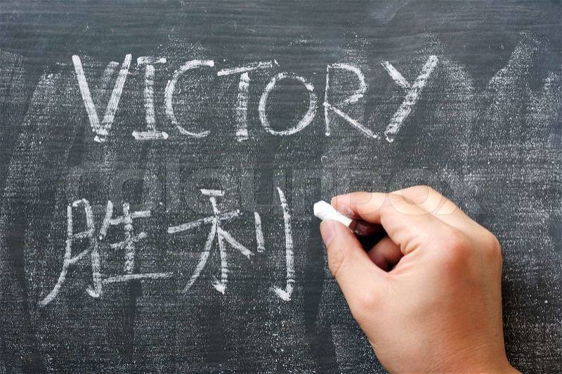 Victory - word written on a blackboard with a Chinese translation, with a hand holding chalk, stock photo