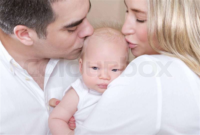 Closeup portrait of young parents kissing beautiful newborn daughter, hug with love, happy parenthood, tenderness concept, stock photo