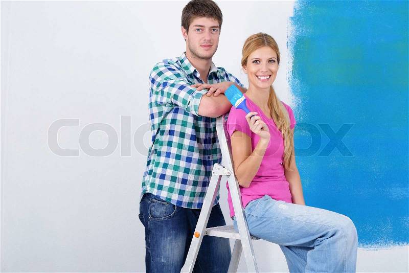 Happy young couple paint in blue color white wall of their new home, stock photo