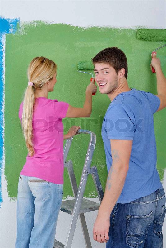 Happy young couple paint in green and blue color white wall of their new home, stock photo