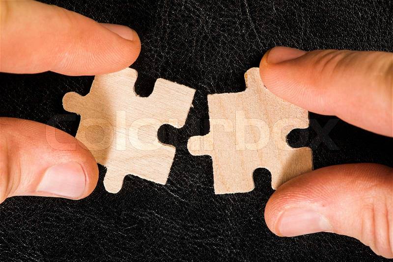 Wooden puzzle on black background. Hand holding puzzle piece, stock photo