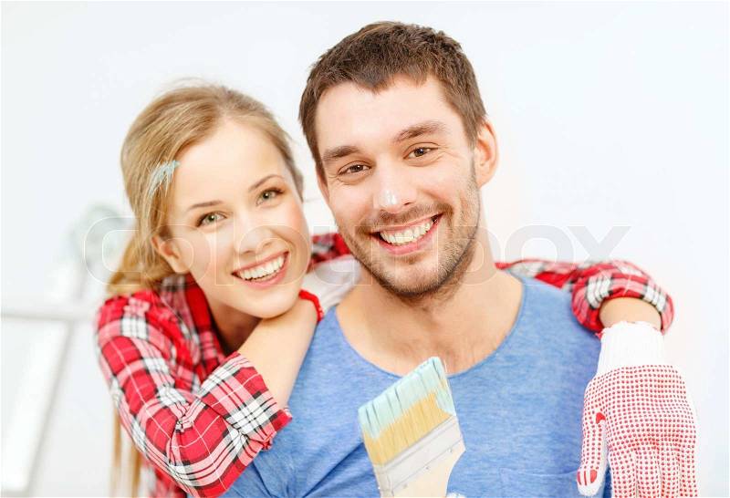 Repair, building and home concept - smiling couple covered with paint with paint brush, stock photo