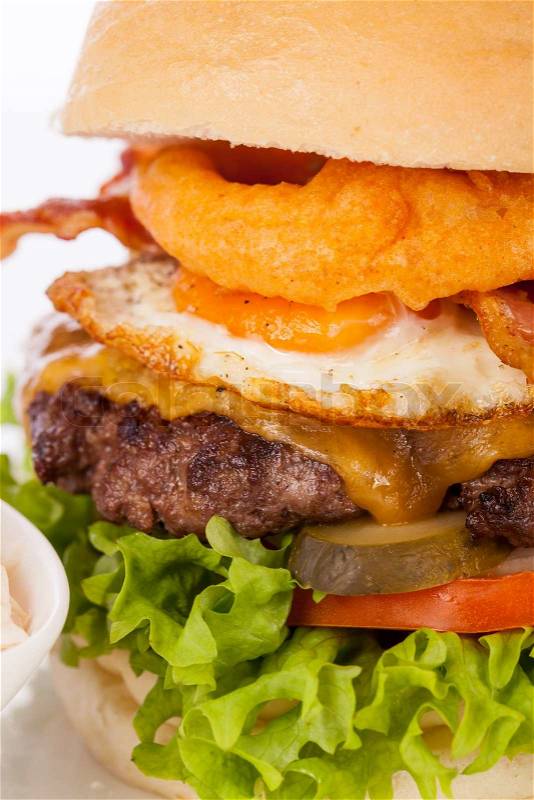Delicious egg and bacon cheeseburger with a nutritional filling of salad ingredients, a ground beef patty, cheese, fried egg and crispy bacon on a white crusty roll, stock photo