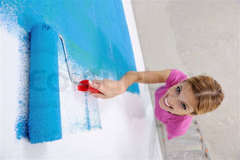 Happy smiling woman painting interior white wall in blue and green color of new house, stock photo
