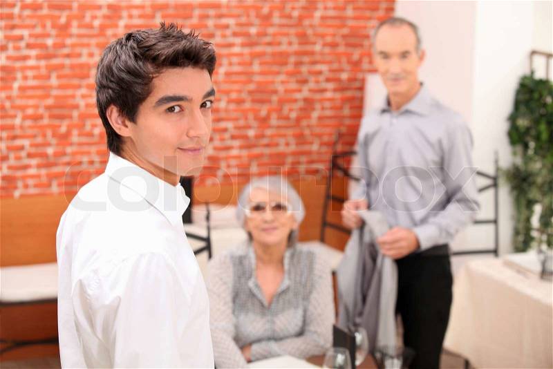Young man looking over his shoulder as a senior couple make to leave a restaurant, stock photo