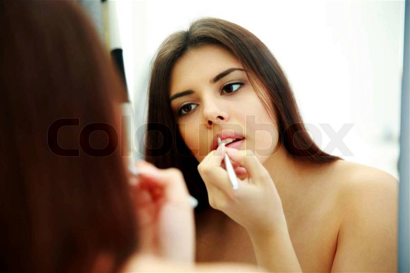 Young beautiful woman looking at mirror while doing makeup, stock photo