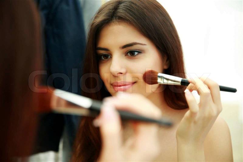 Young beautiful woman looking at mirror while doing makeup , stock photo