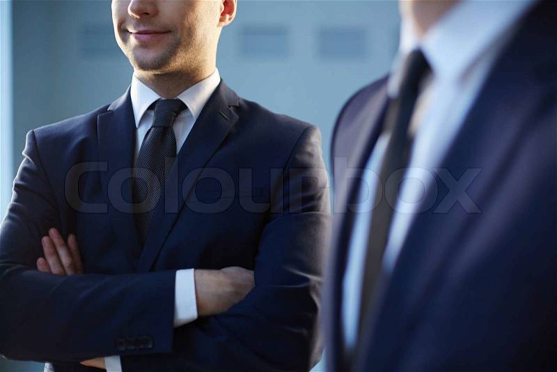Cropped image of a confident businessman standing near his colleague on the foreground , stock photo