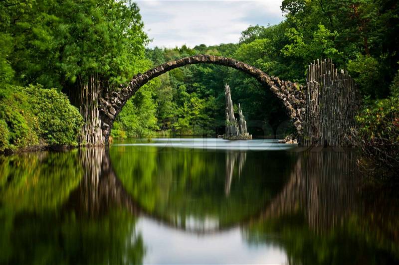 Very old stone bridge over the quiet lake with its reflection in the water, long exposure, stock photo