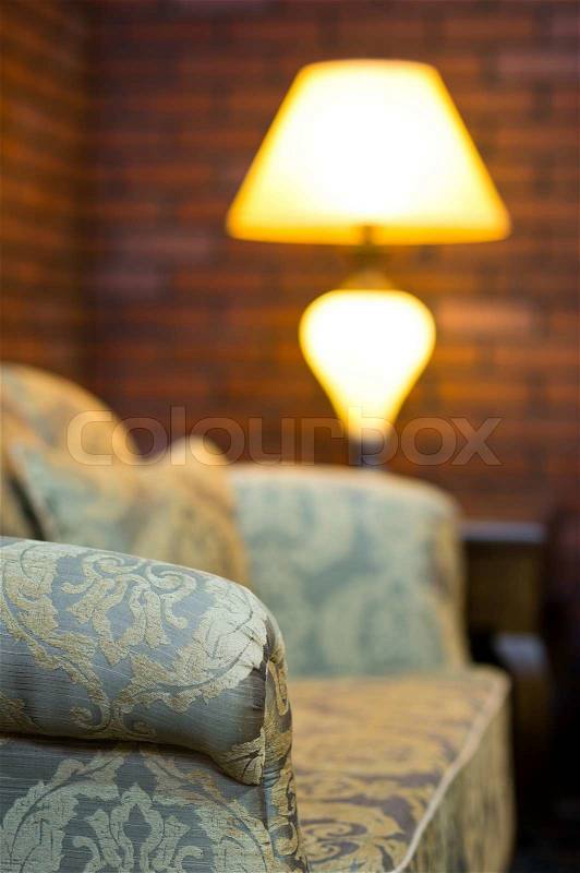 Old sofa in a room with lamp and red brick wall decor, stock photo
