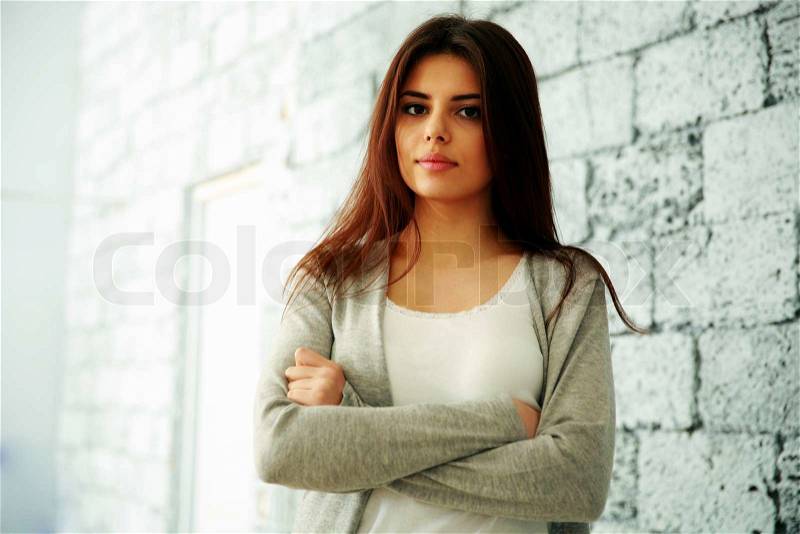 Young happy woman with arms folded standing near brick wall, stock photo