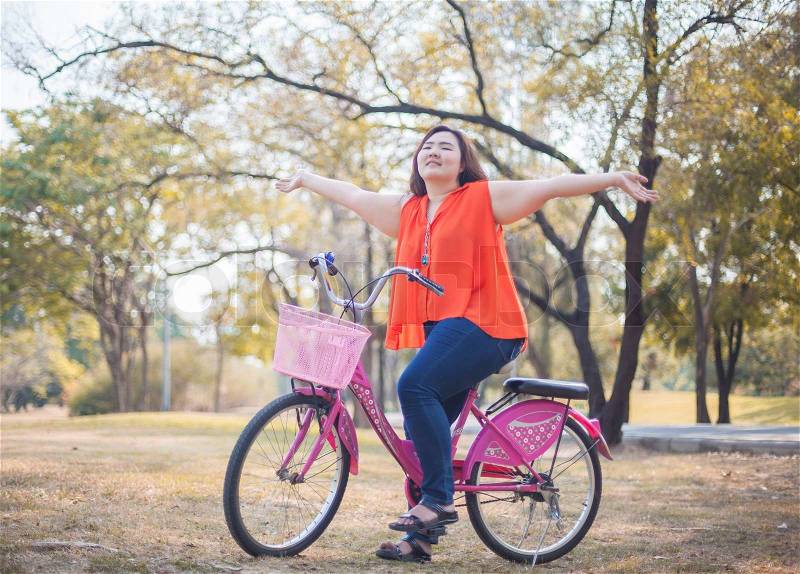 Happy fatty asian woman outstretched with bicycle outdoor in a park, stock photo
