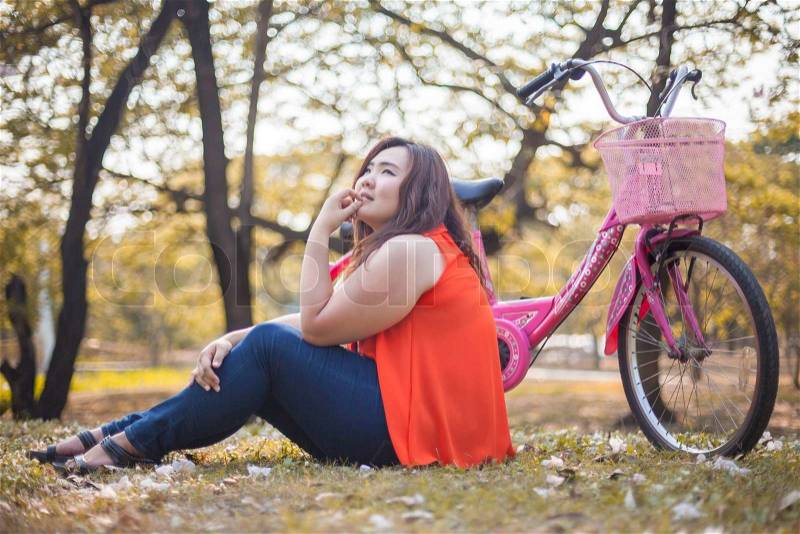 Happy fatty asian woman posing with bicycle outdoor in a park, stock photo