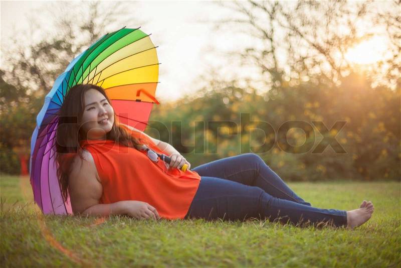 Happy fatty asian woman with umbrella outdoor in a park, stock photo