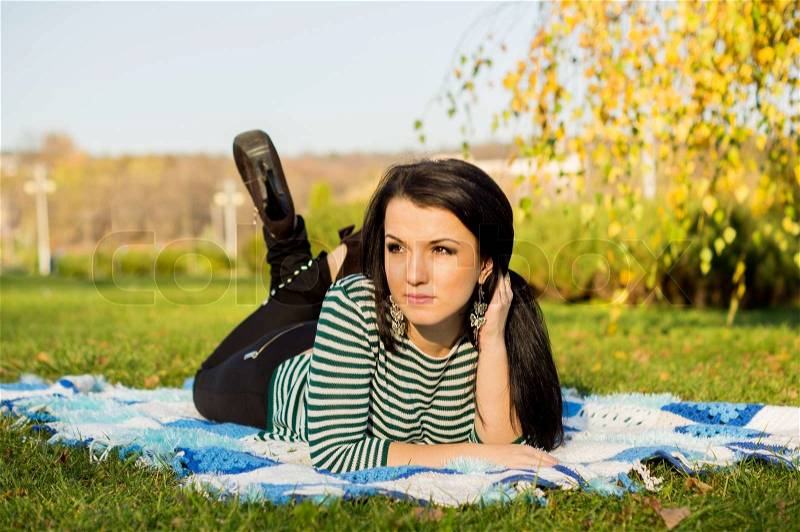 Young woman laying down on the ground in autumn park, stock photo