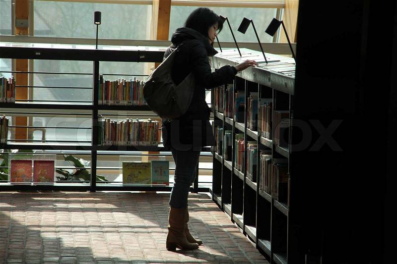 The lady with shoulder bag is searching her favorite book between all kind of books in the municipal library, stock photo