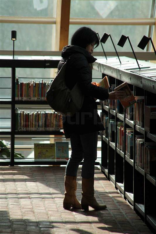 The lady with her shoulder bag find her favorite book between all the books in the municipal library, stock photo
