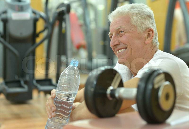 Elderly man in a gym drinking water after exercise, stock photo