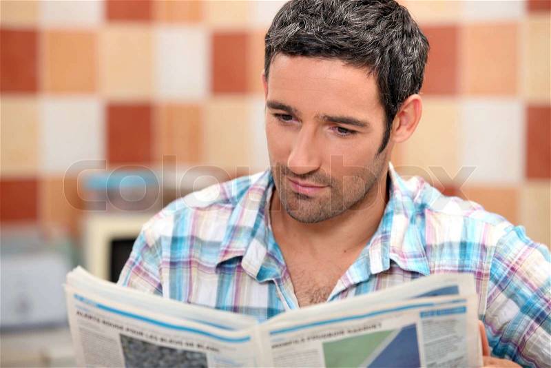 Man reading a journal in the kitchen, stock photo