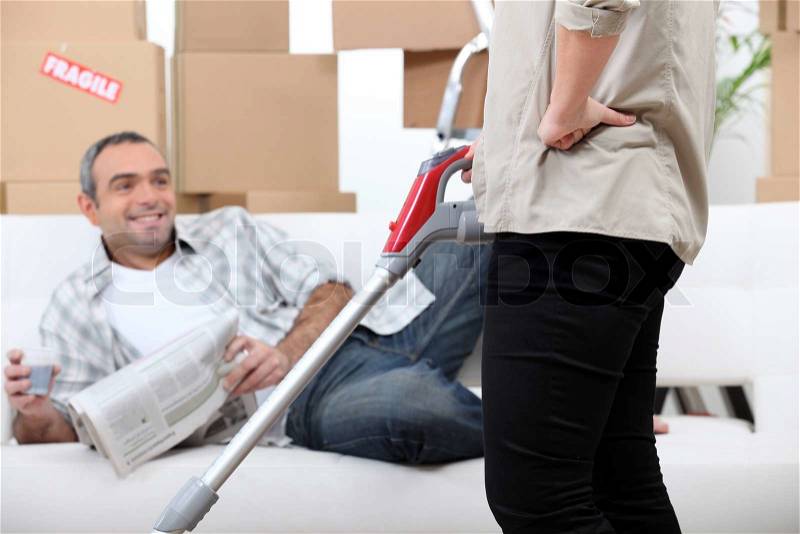 Lazy man watching his wife vacuum, stock photo