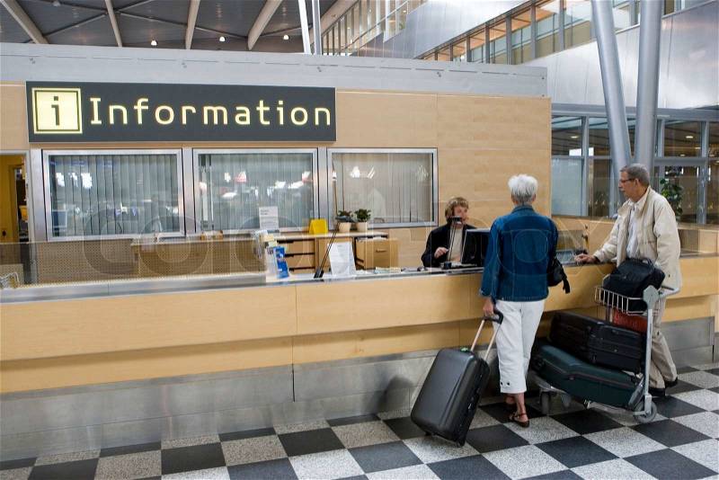 An elderly couple in front of an information counter at the airport, stock photo