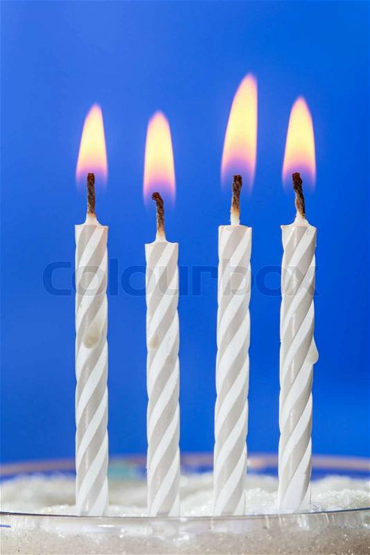 Four white birthday candles burning over blue background, stock photo