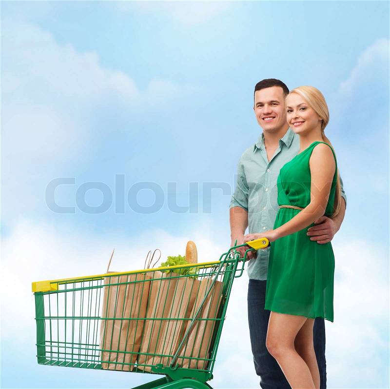 Happiness, shopping and couple concept - smiling couple with shopping cart and food in it, stock photo