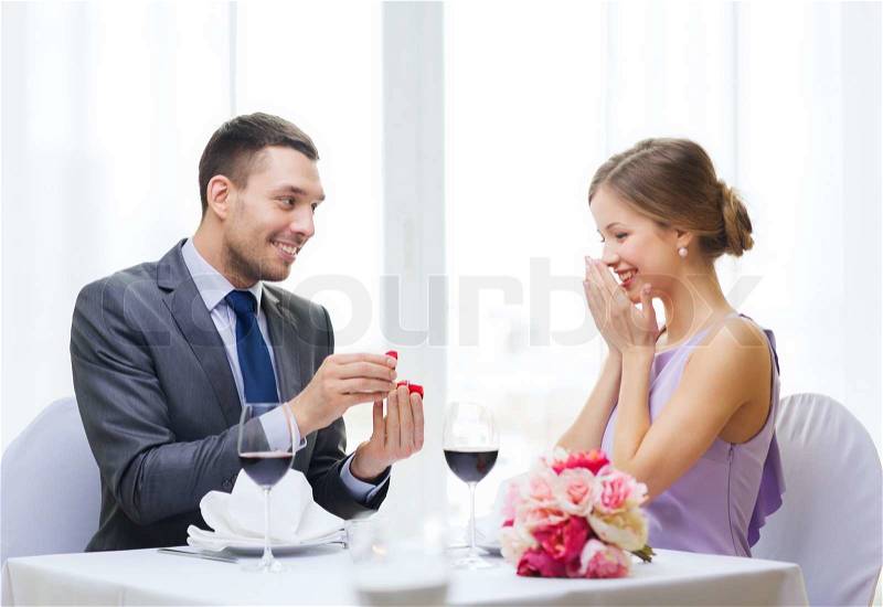 Restaurant, couple and holiday concept - smiling man proposing to his girlfriend at restaurant, stock photo