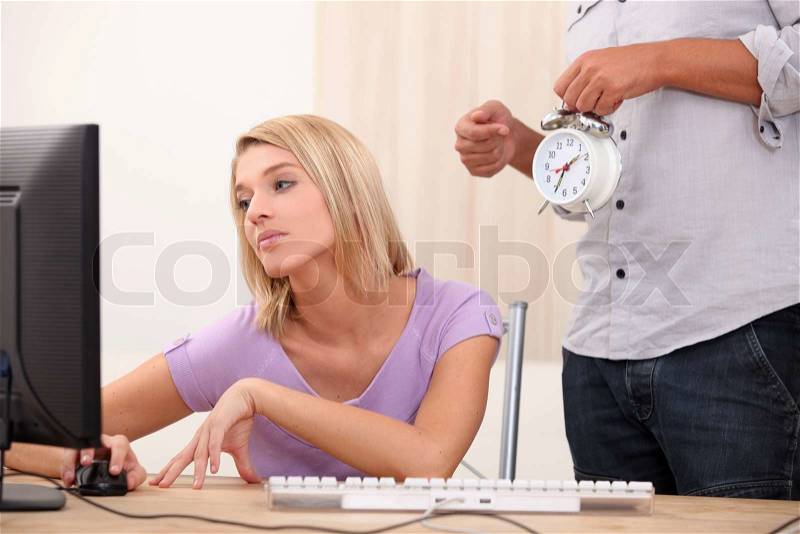A young blonde woman is doing computer and a man is showing an alarm clock, stock photo