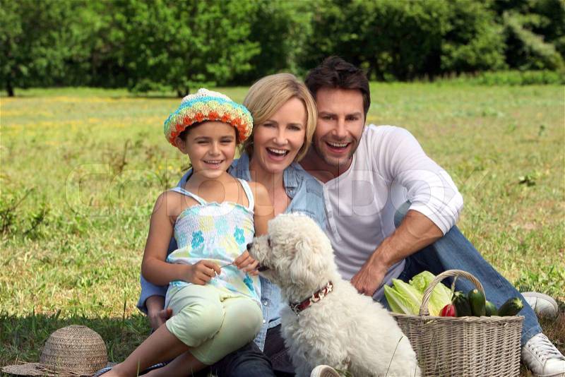 Parents and young daughter with dog and basket of vegetables, stock photo
