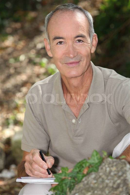 Senior man writing in the countryside, stock photo