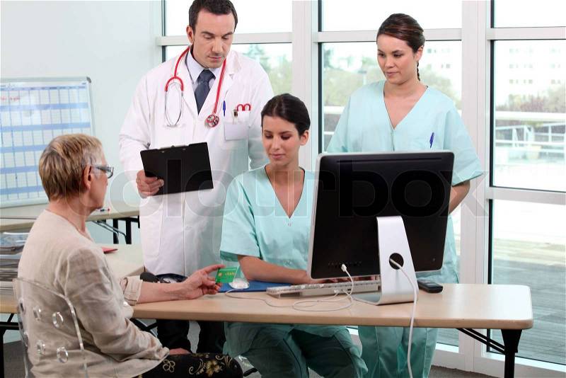 Doctor, patient, and medical secretaries at reception, stock photo